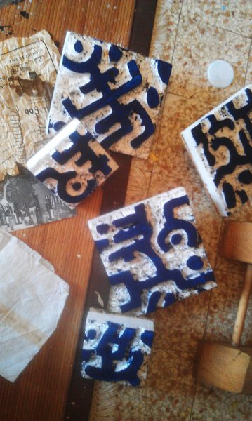 Timbri inchiostrati di blu scuro sparsi su un pavimento macchiato di colore, accanto a fogli di giornale e a un mazzuolo di legno.